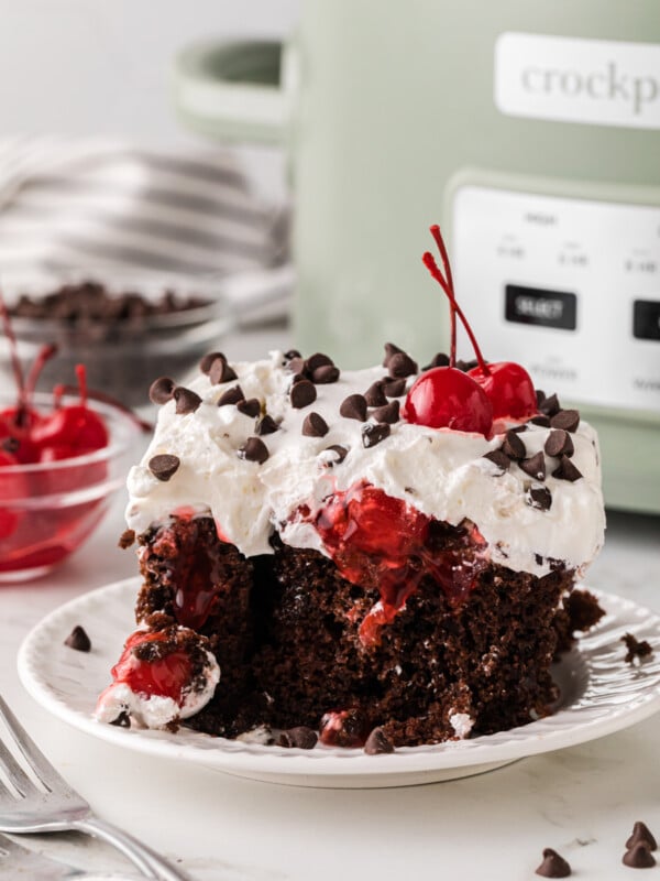 A slice of black forest cake on a plate in front of a crockpot.