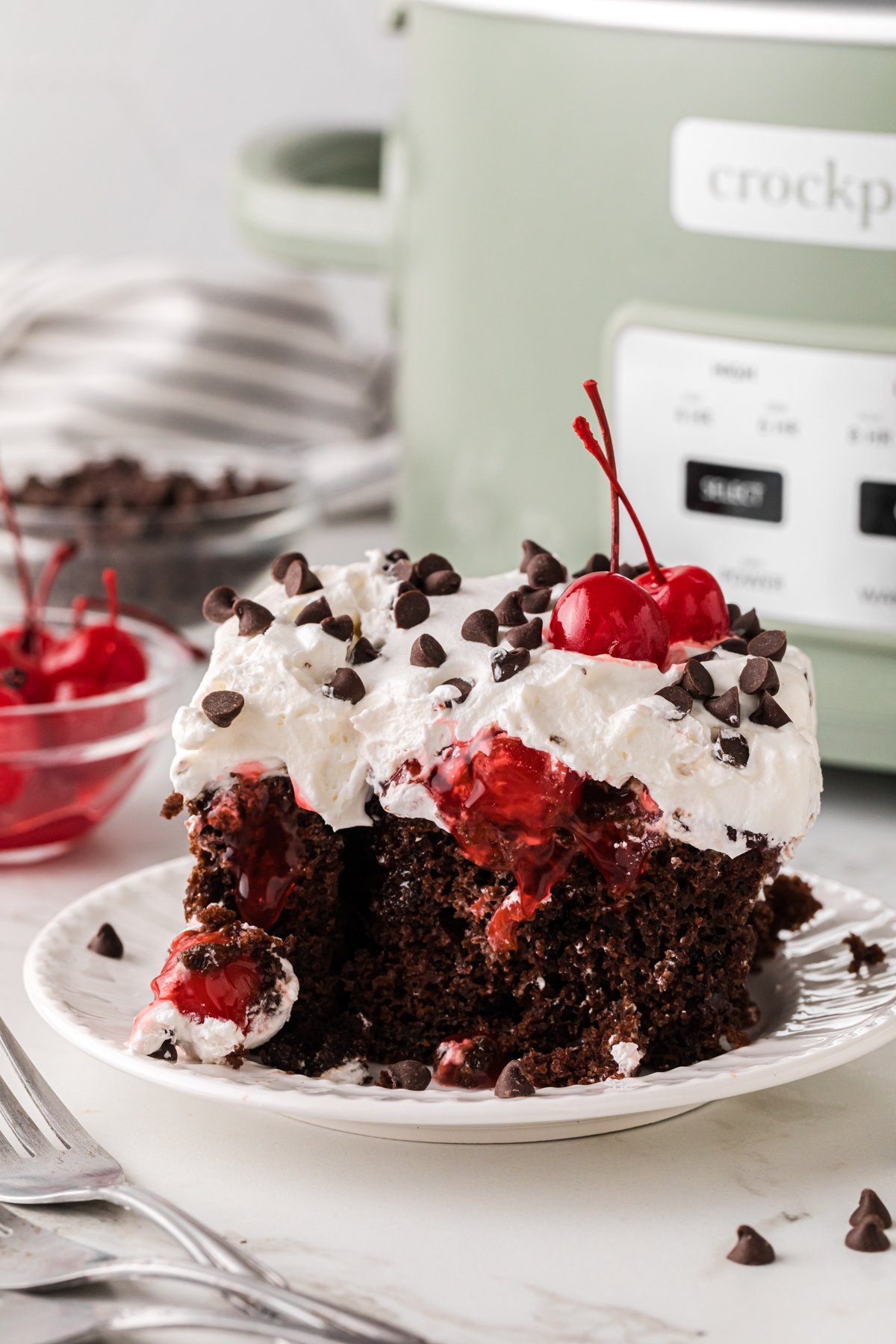 A slice of black forest cake on a plate in front of a crockpot.
