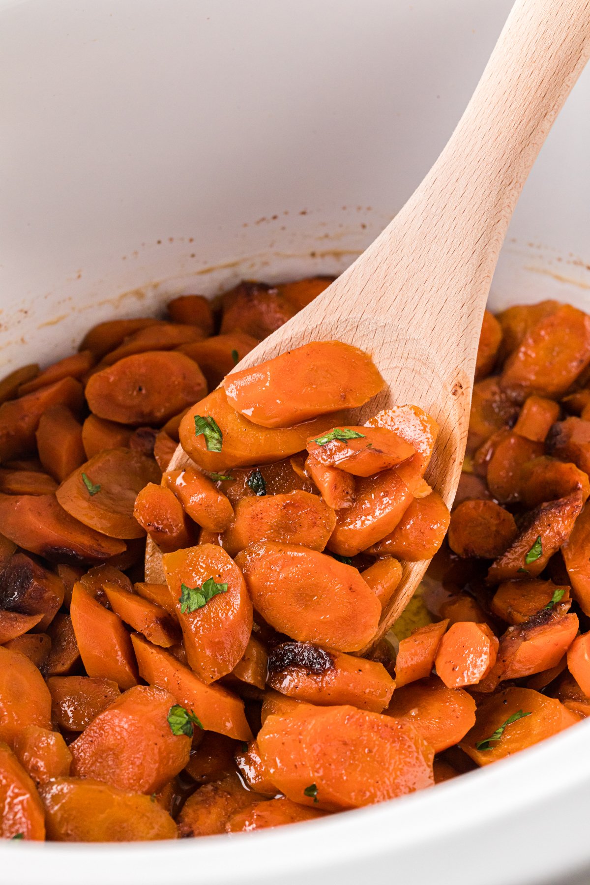 A wooden spoon holding some brown sugar carrots in a crockpot.