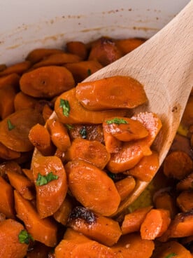Sliced carrots in a crockpot with a wooden spoon scooping some out.