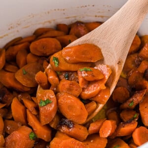Sliced carrots in a crockpot with a wooden spoon scooping some out.