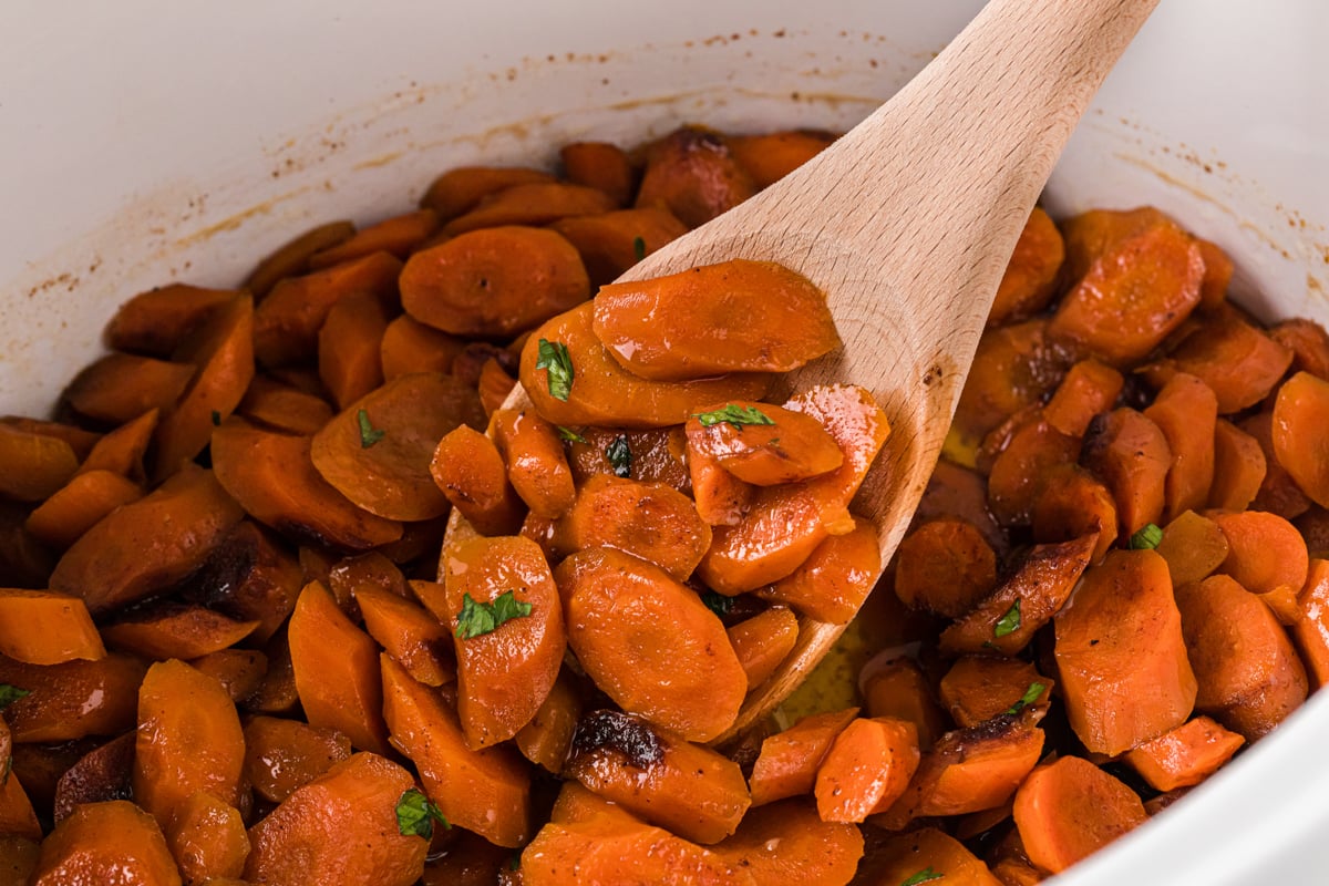 Sliced carrots in a crockpot with a wooden spoon scooping some out.