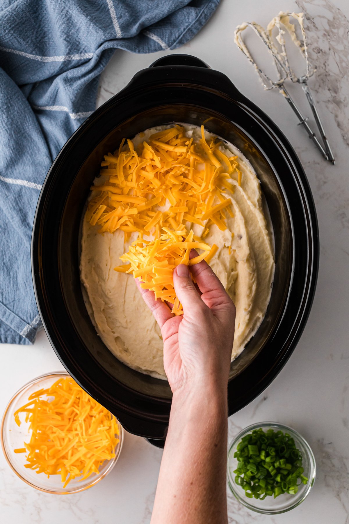 Adding cheese to mashed potatoes in a crockpot.