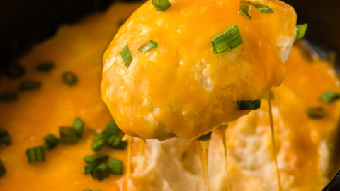 A spoon pulling cheesy mashed potatoes out of a crockpot.