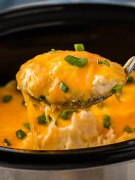 Mashed potatoes in a crockpot being scooped out with a large spoon.