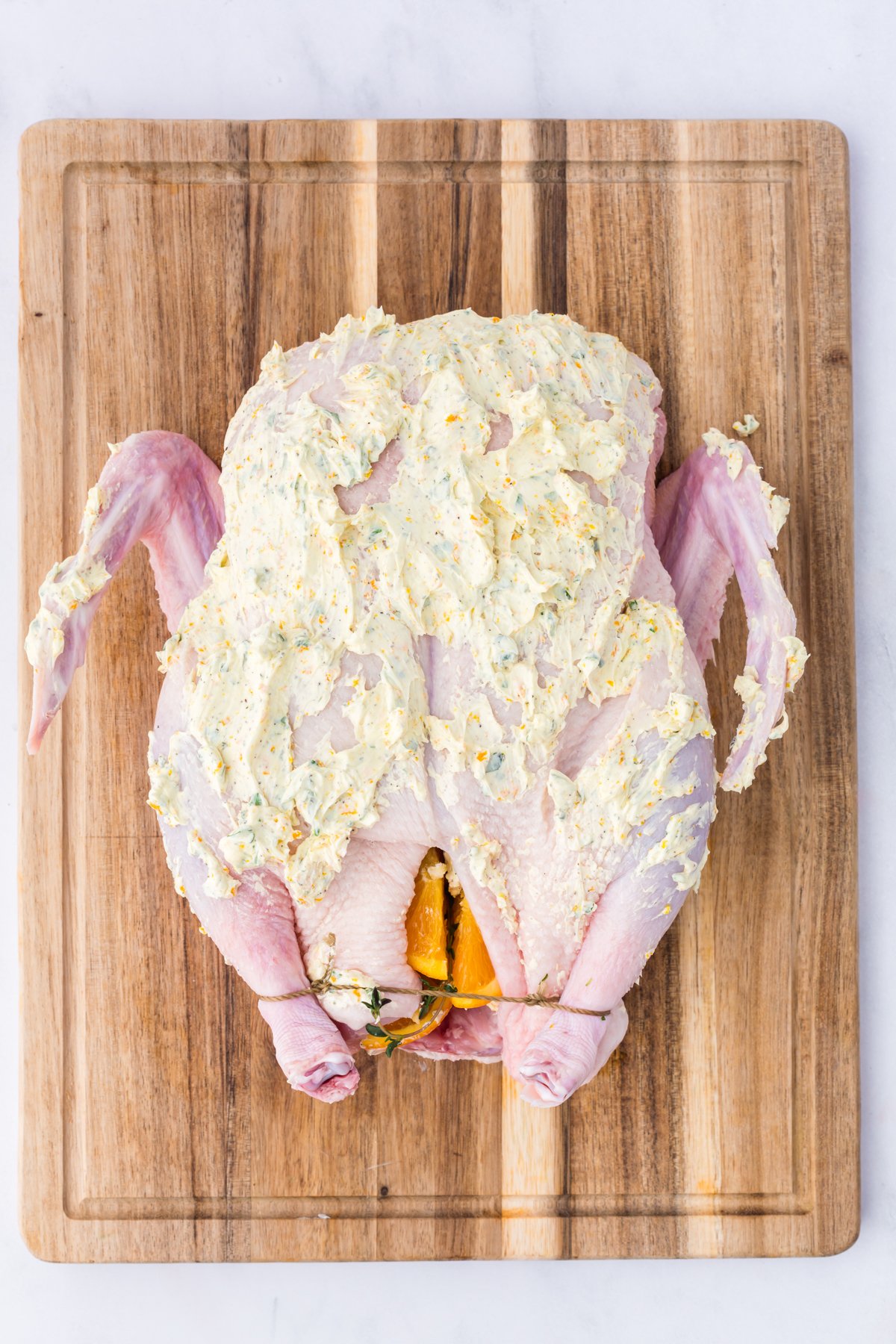 Whole duck with an herb butter rub on a wooden board.