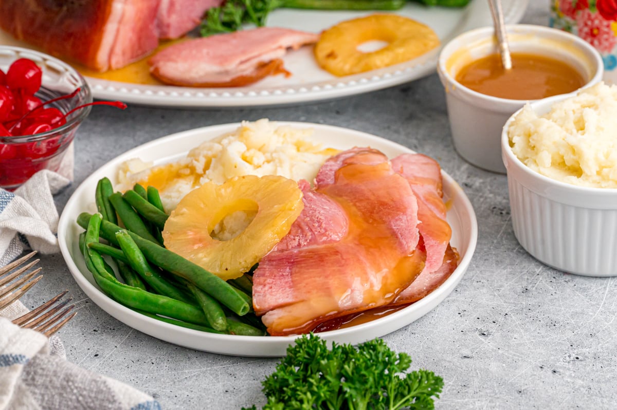 A serving of ham with mashed potatoes and green beans on a white plate.