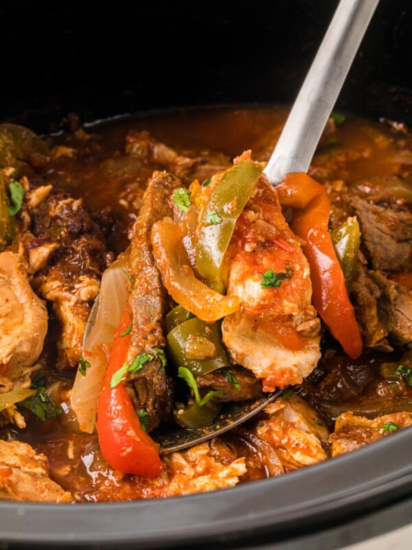 A spoon holding a scoop of chicken and steak fajita mixture.