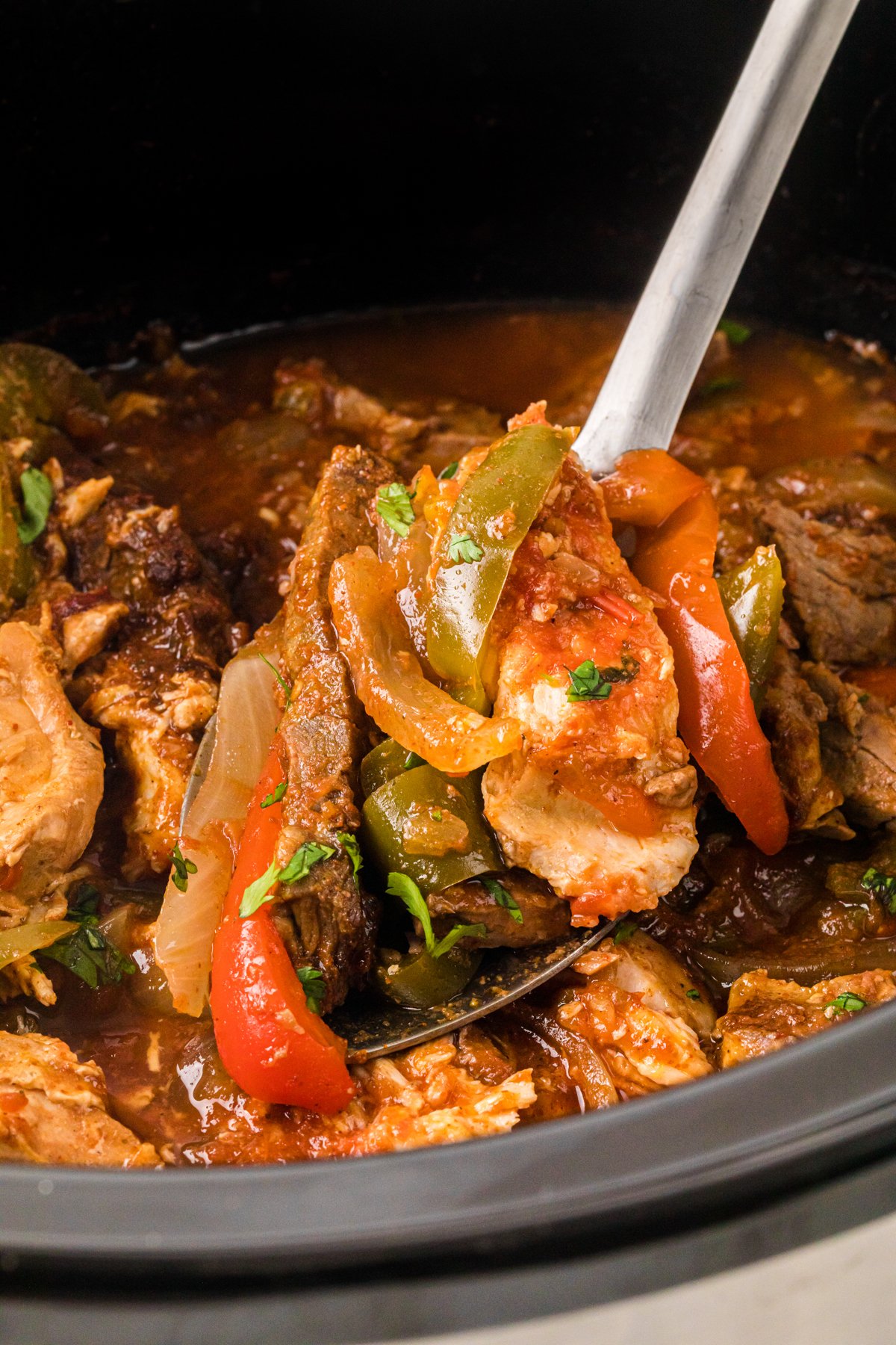 A spoon holding a scoop of chicken and steak fajita mixture.