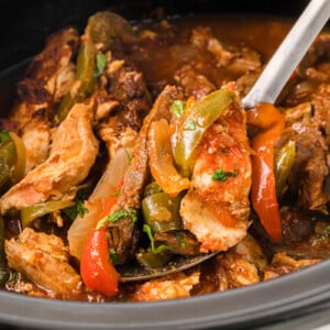 A spoon taking a scoop of fajita meat and veggies from a crockpot.