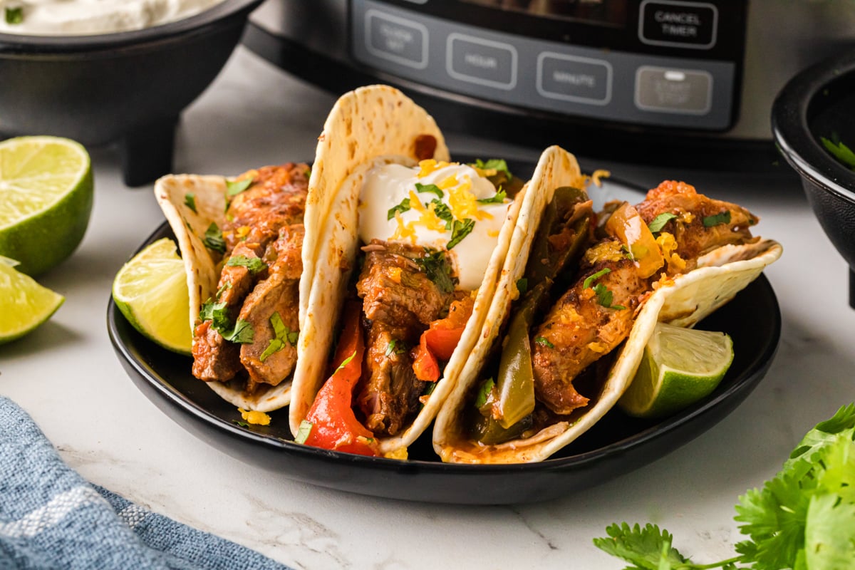 Three chicken and steak fajitas in front of a slow cooker.