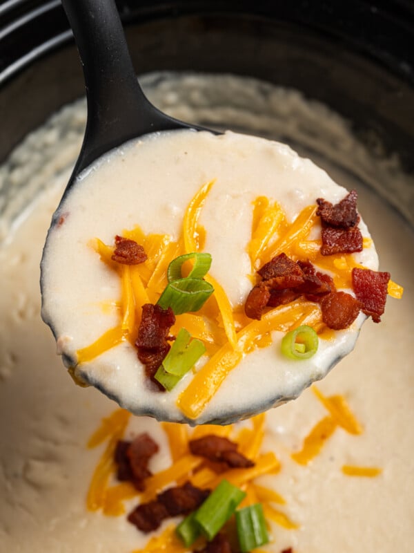Close-up of a ladleful of creamy soup with cheese, bacon, and green onions.