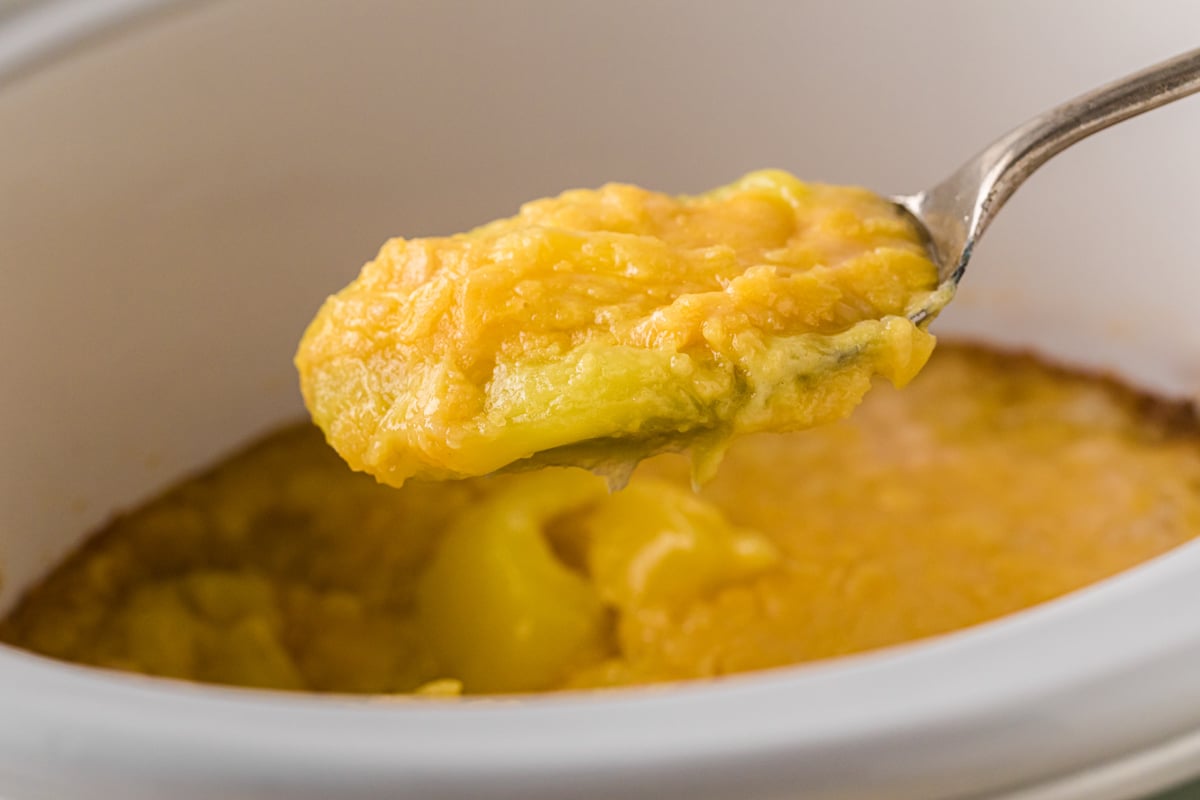 A spoon holding a scoop of lemon dump cake over a crockpot.