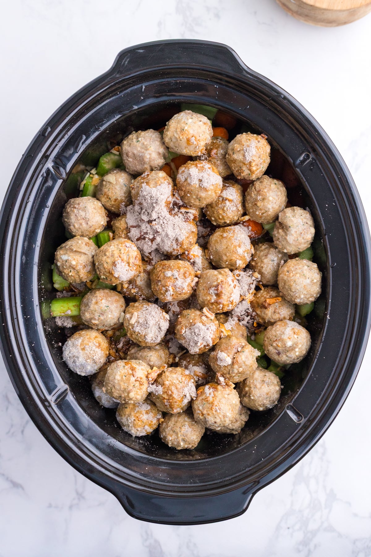 Seasonings added to meatballs and veggies in a slow cooker.