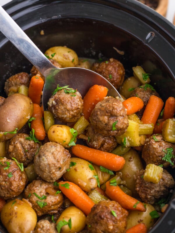 A large spoon scooping out some meatballs and veggies from a crockpot.