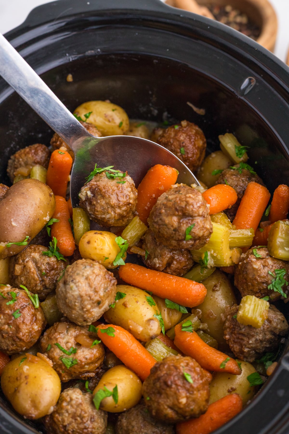 A large spoon scooping out some meatballs and veggies from a crockpot.