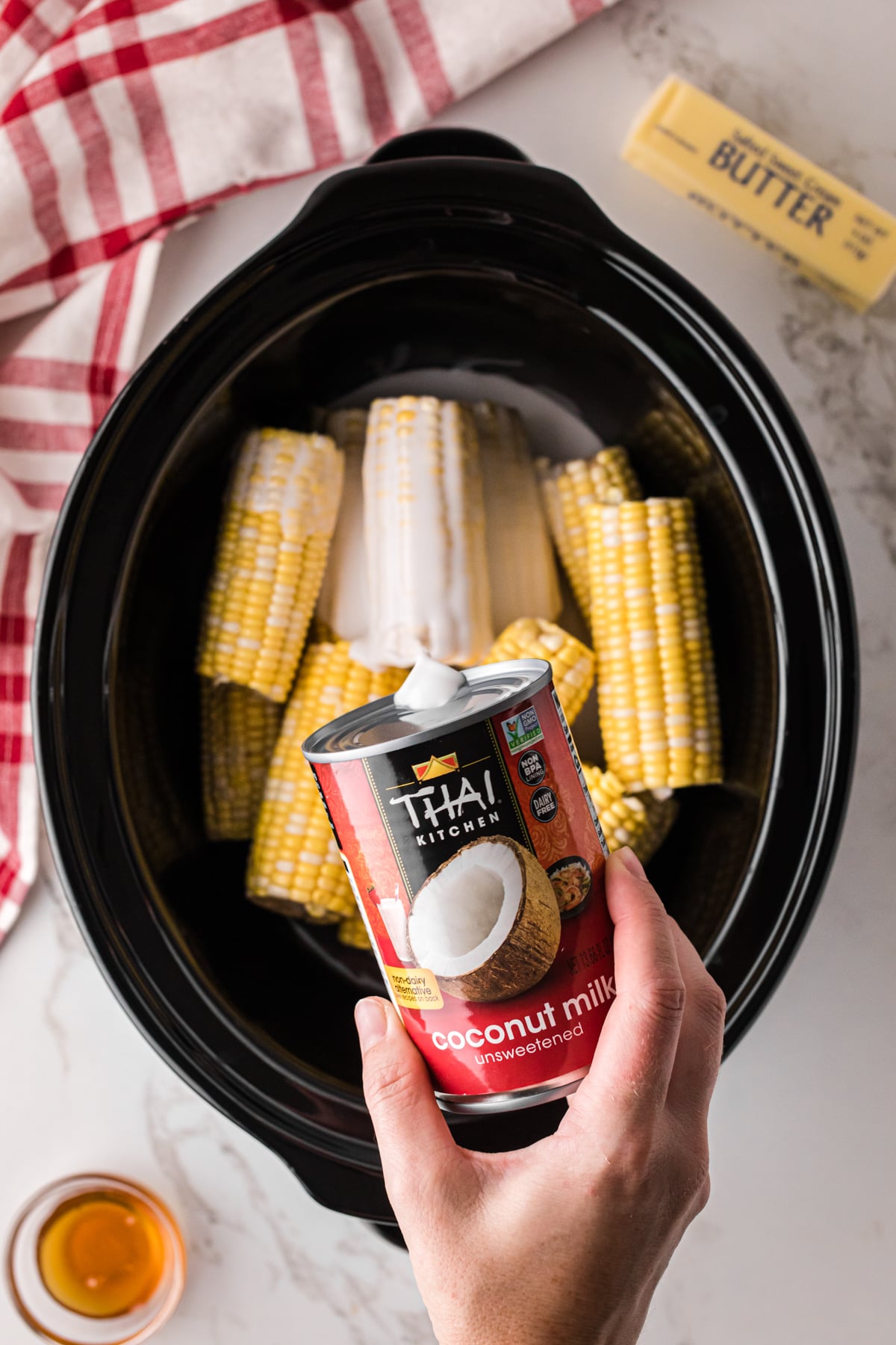 Pouring coconut milk onto ears of corn in a crockpot.