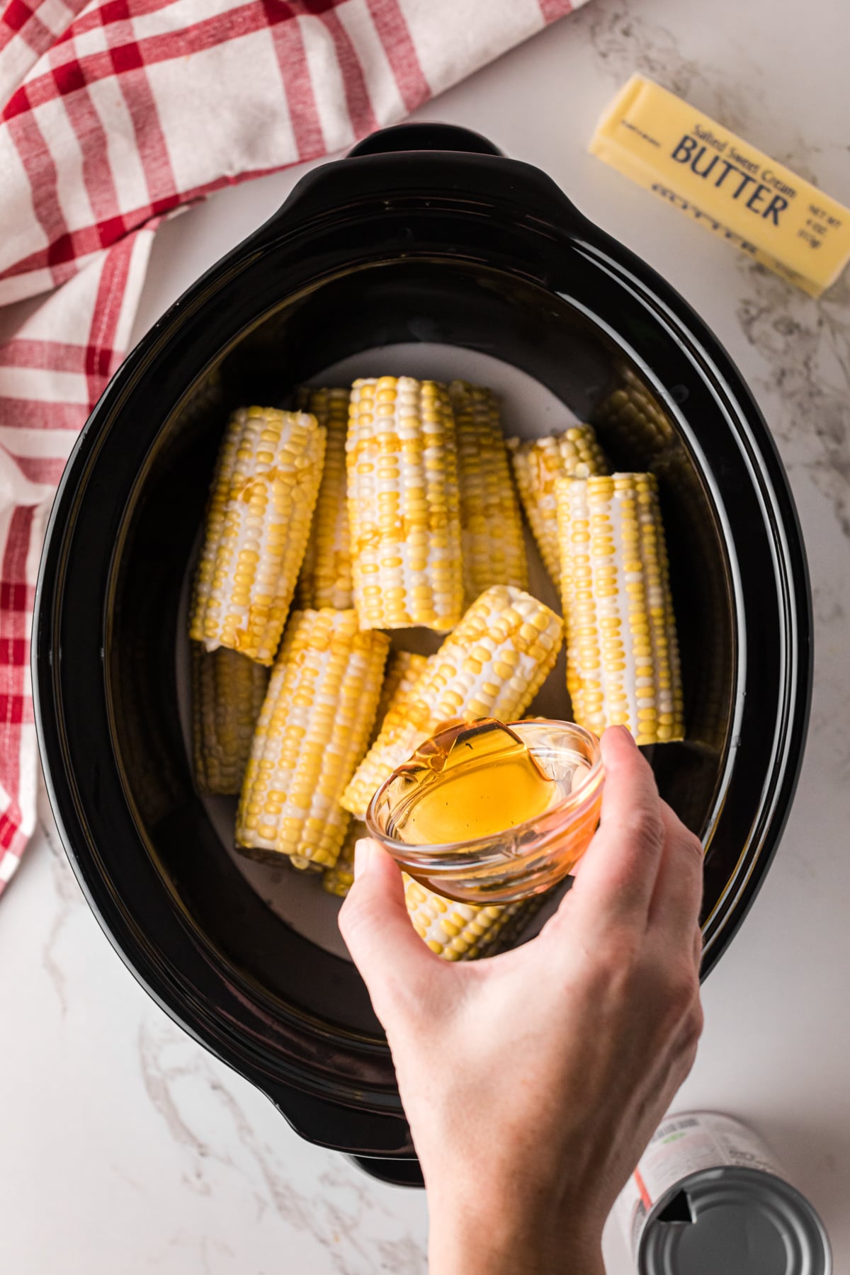 Pouring honey onto ears of corn in a crockpot.