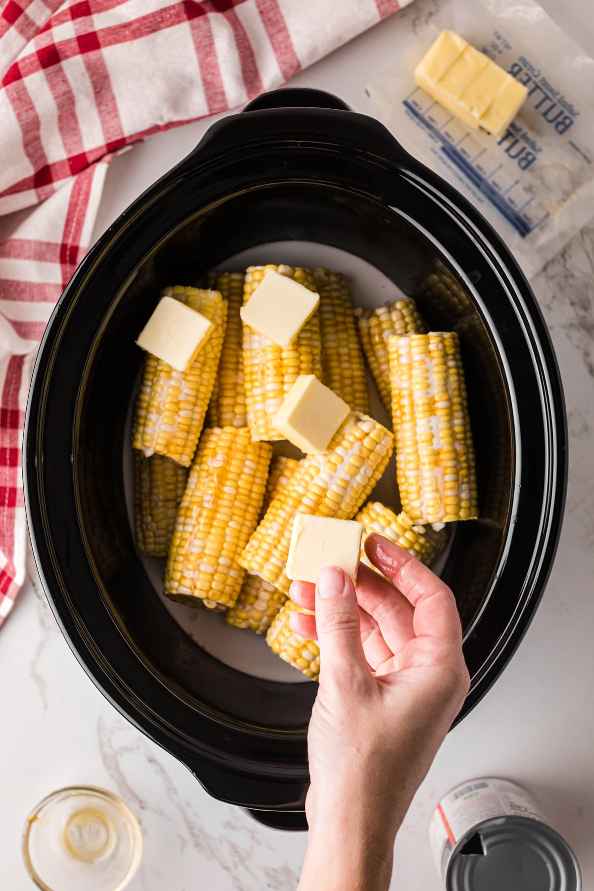 Placing pats of butter onto ears of corn in a crockpot.