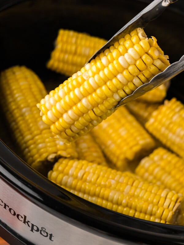 Tongs holding an ear of corn over a crockpot.