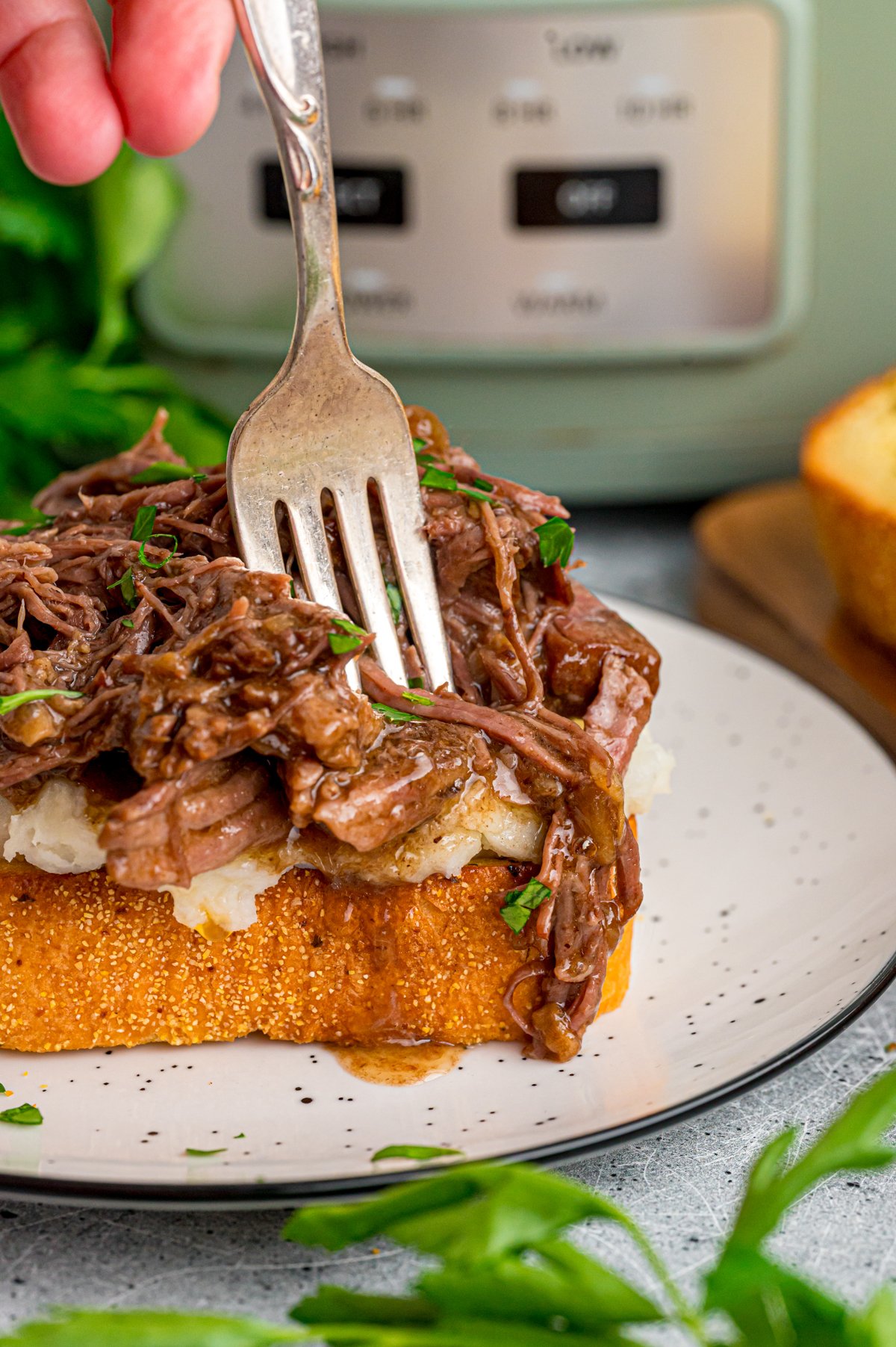 A hand holding a fork going into a piece of beef manhattan toast.