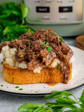 A serving of beef manhattan on a plate in front of a crockpot.