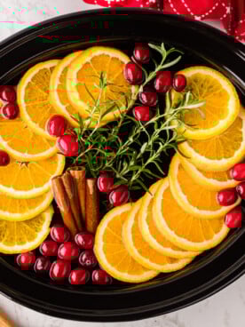 Orange slices, cranberries, rosemary, and cinnamon sticks in a slow cooker.