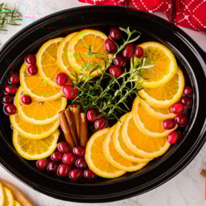 Orange slices, cranberries, rosemary, and cinnamon sticks in a slow cooker.