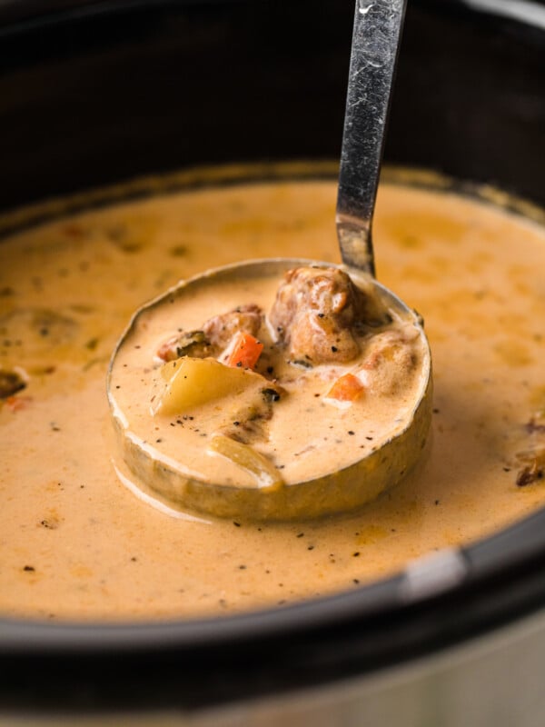 A ladle of beef and cheddar soup coming out of a crockpot.