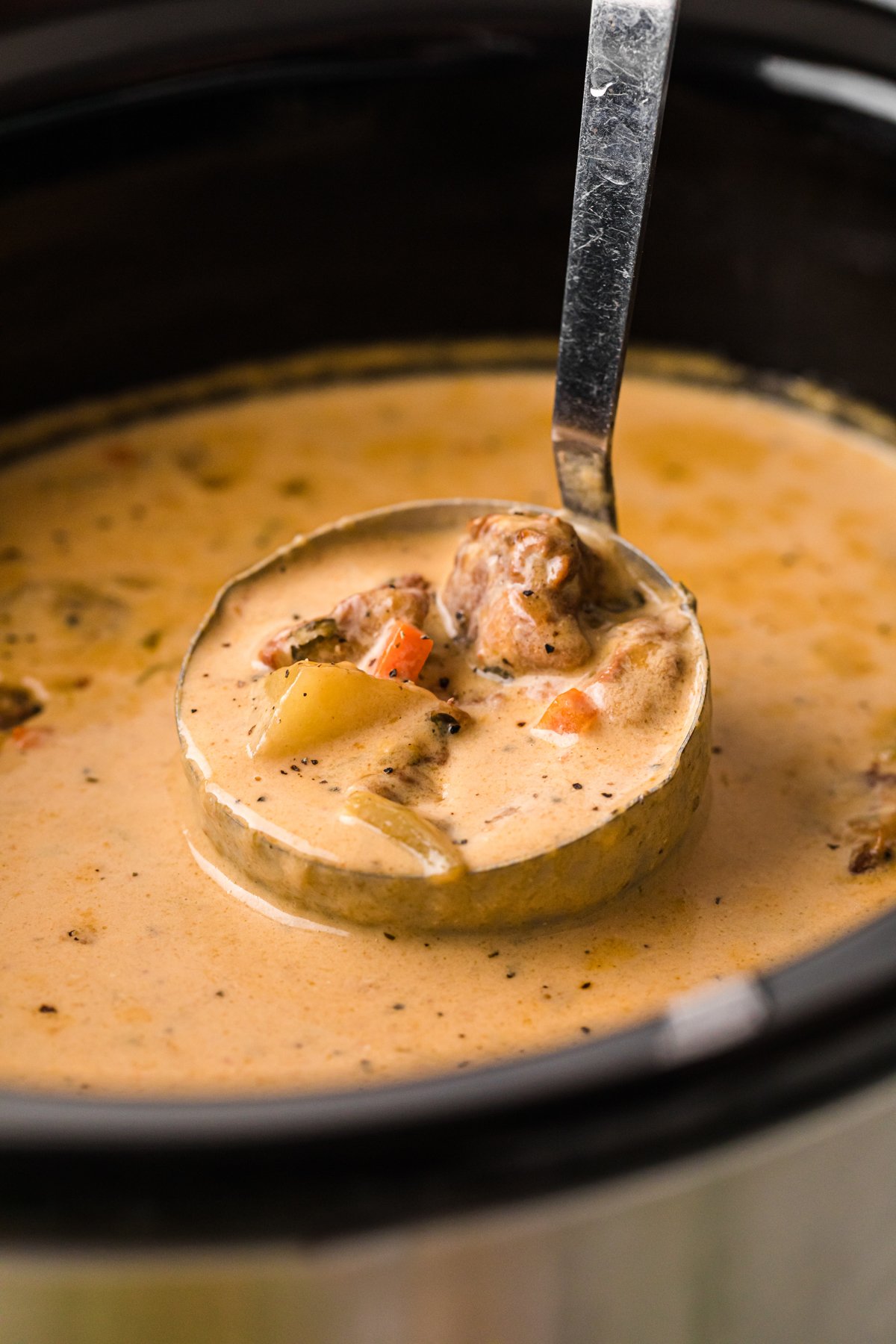 A ladle of beef and cheddar soup coming out of a crockpot.