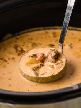 A crockpot of soup with a ladle scooping some out.
