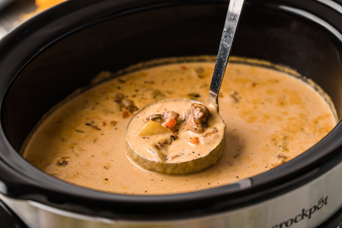 A crockpot of soup with a ladle scooping some out.