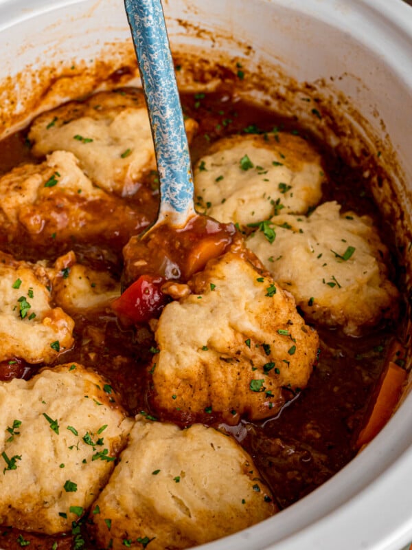 A large spoon scooping some beef stew with dumplings from a crockpot.