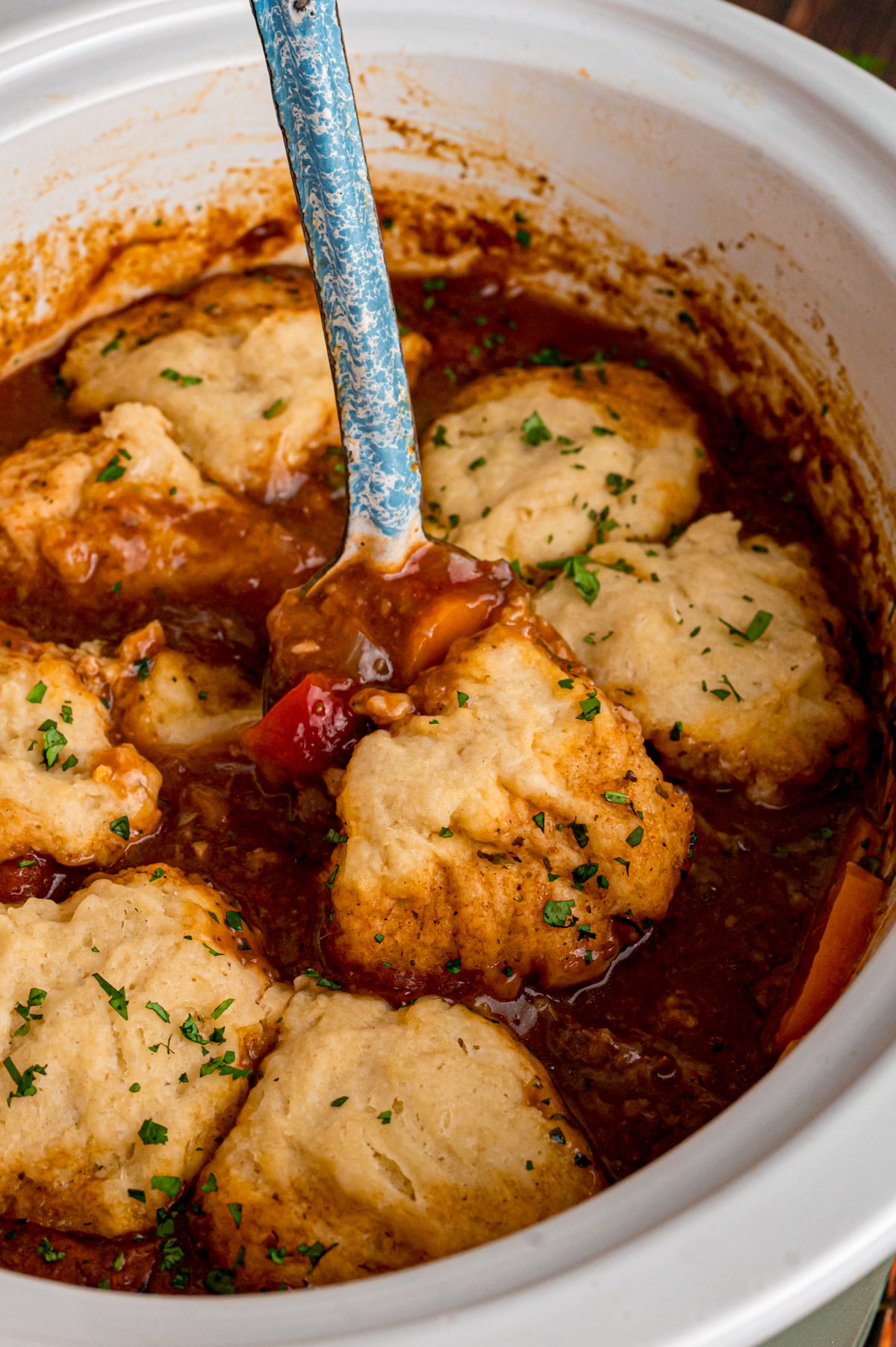 A large spoon scooping some beef stew with dumplings from a crockpot.
