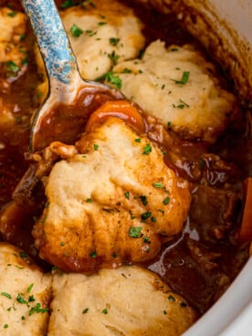 Some beef stew and a dumpling being scooped from a crockpot.