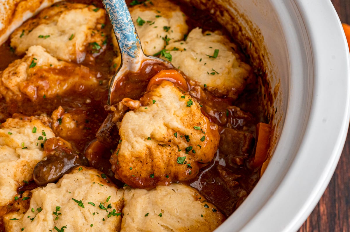 Some beef stew and a dumpling being scooped from a crockpot.