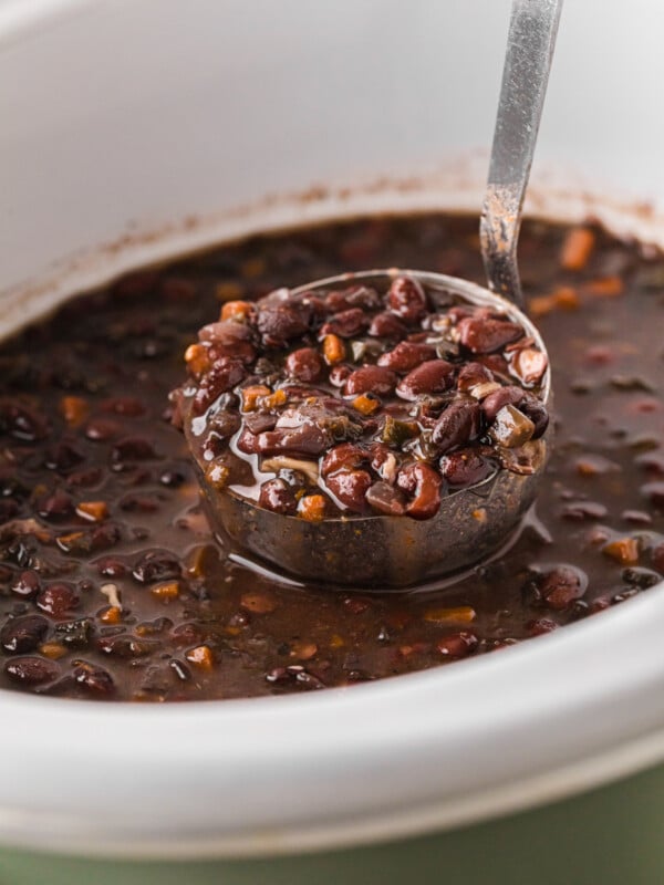 A ladle of Cuban black beans being held over a crockpot.