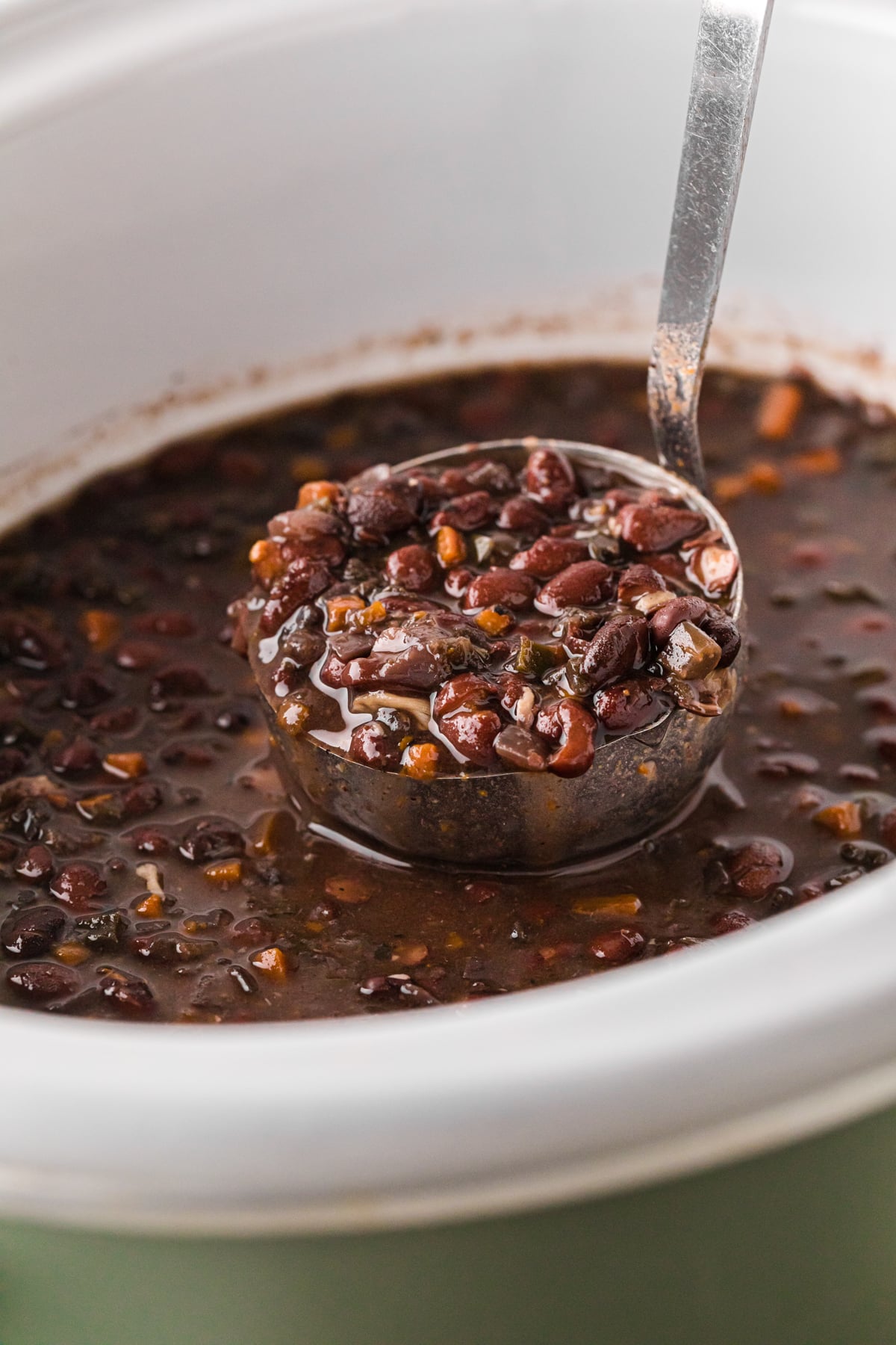 A ladle of Cuban black beans being held over a crockpot.
