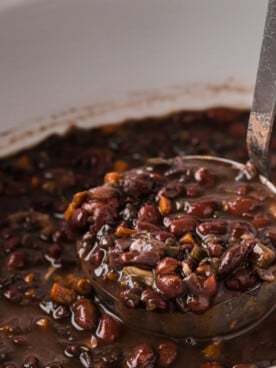 Scooping black beans out of a slow cooker with a ladle.