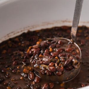 Scooping black beans out of a slow cooker with a ladle.