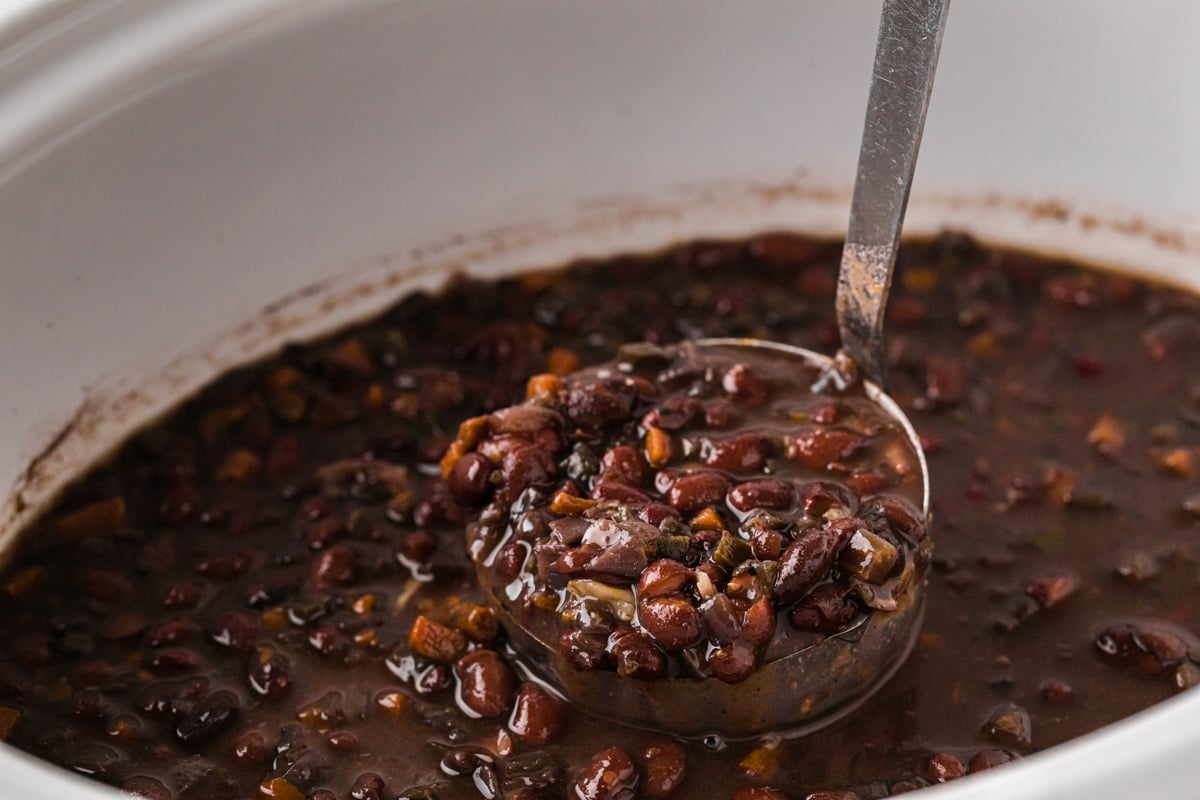 Scooping black beans out of a slow cooker with a ladle.