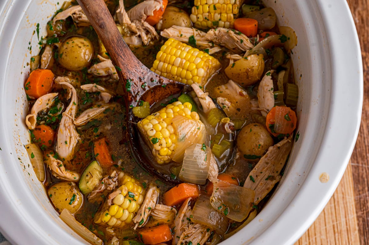 A wooden spoon grabbing some caldo de pollo from a crockpot.