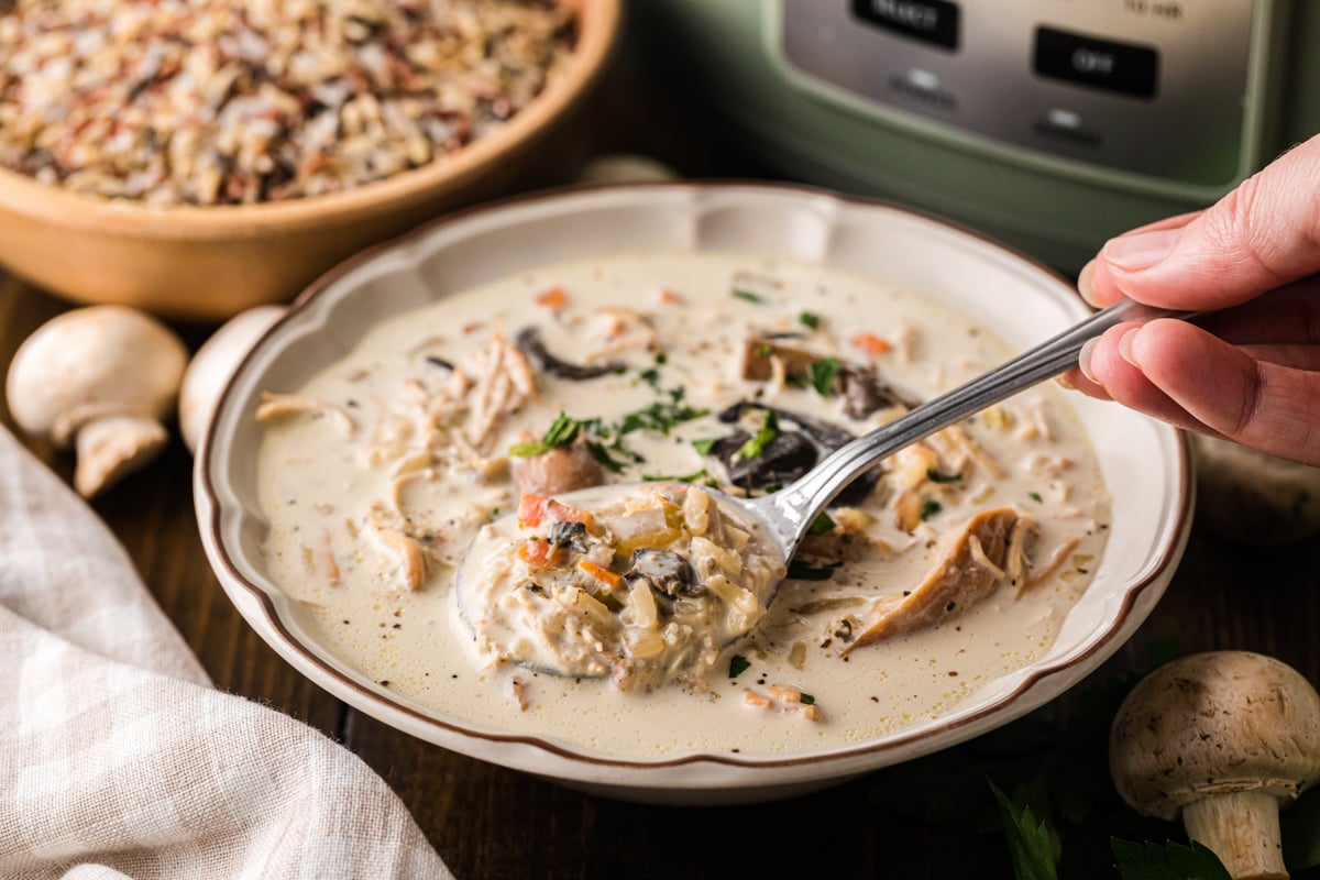A hand holding a spoon scooping soup from a bowl.