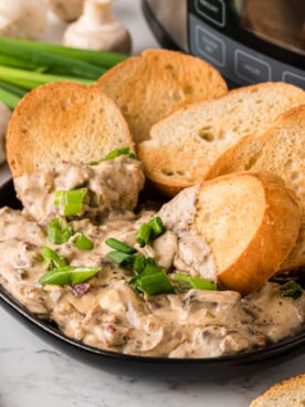 Stuffed mushroom dip in a serving bowl with toasted bread pieces in it.