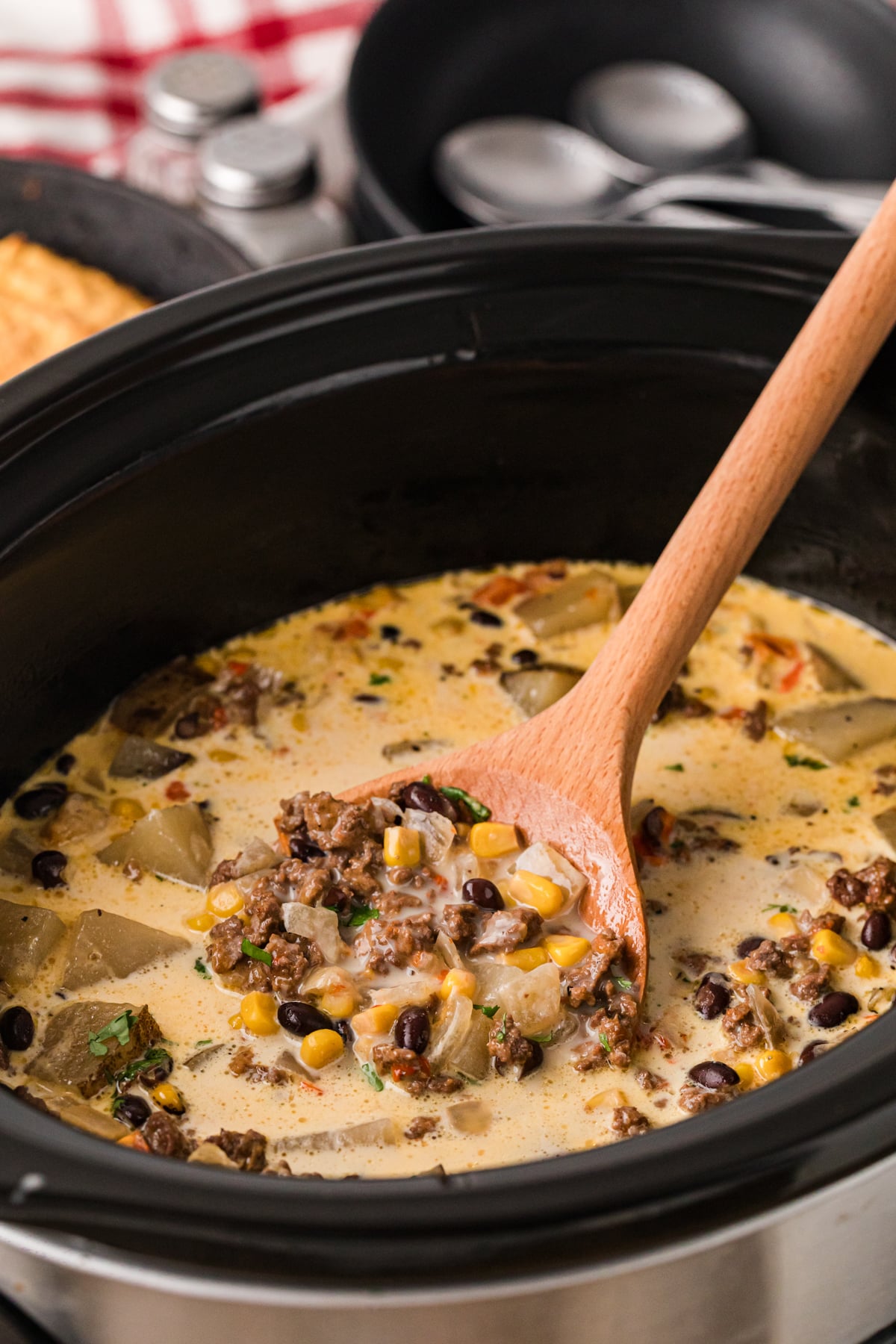 A wooden spoon scooping cowgirl soup from a crockpot.