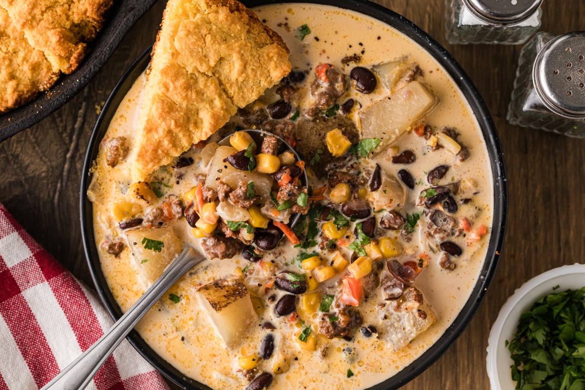 Cowgirl soup in a bowl with a spoon and a piece of cornbread in it.