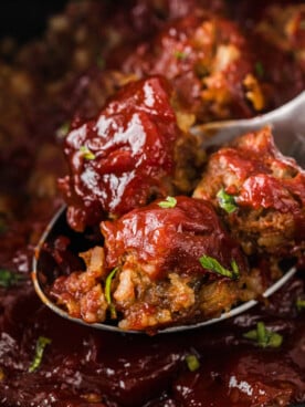 Meatballs on a metal spoon being pulled out of a crockpot.