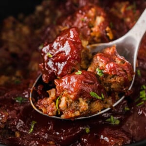 Meatballs on a metal spoon being pulled out of a crockpot.