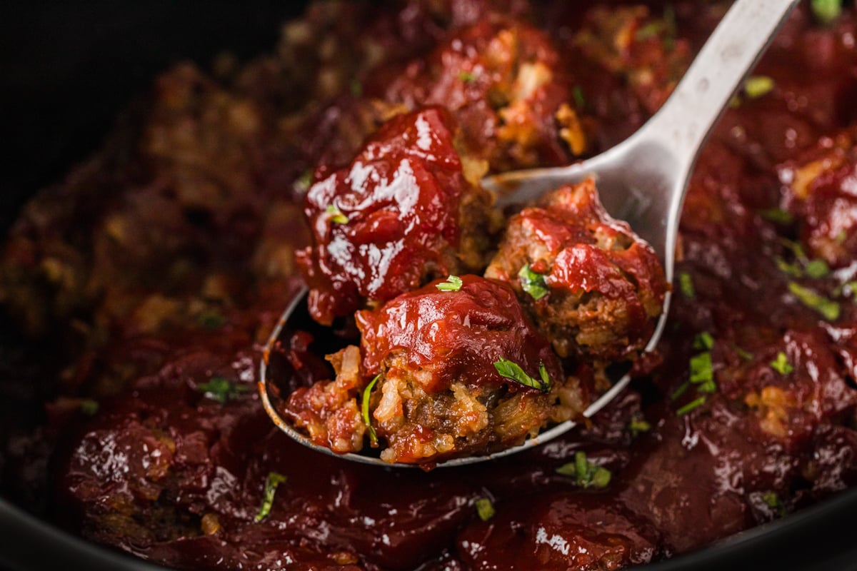 Meatballs on a metal spoon being pulled out of a crockpot.