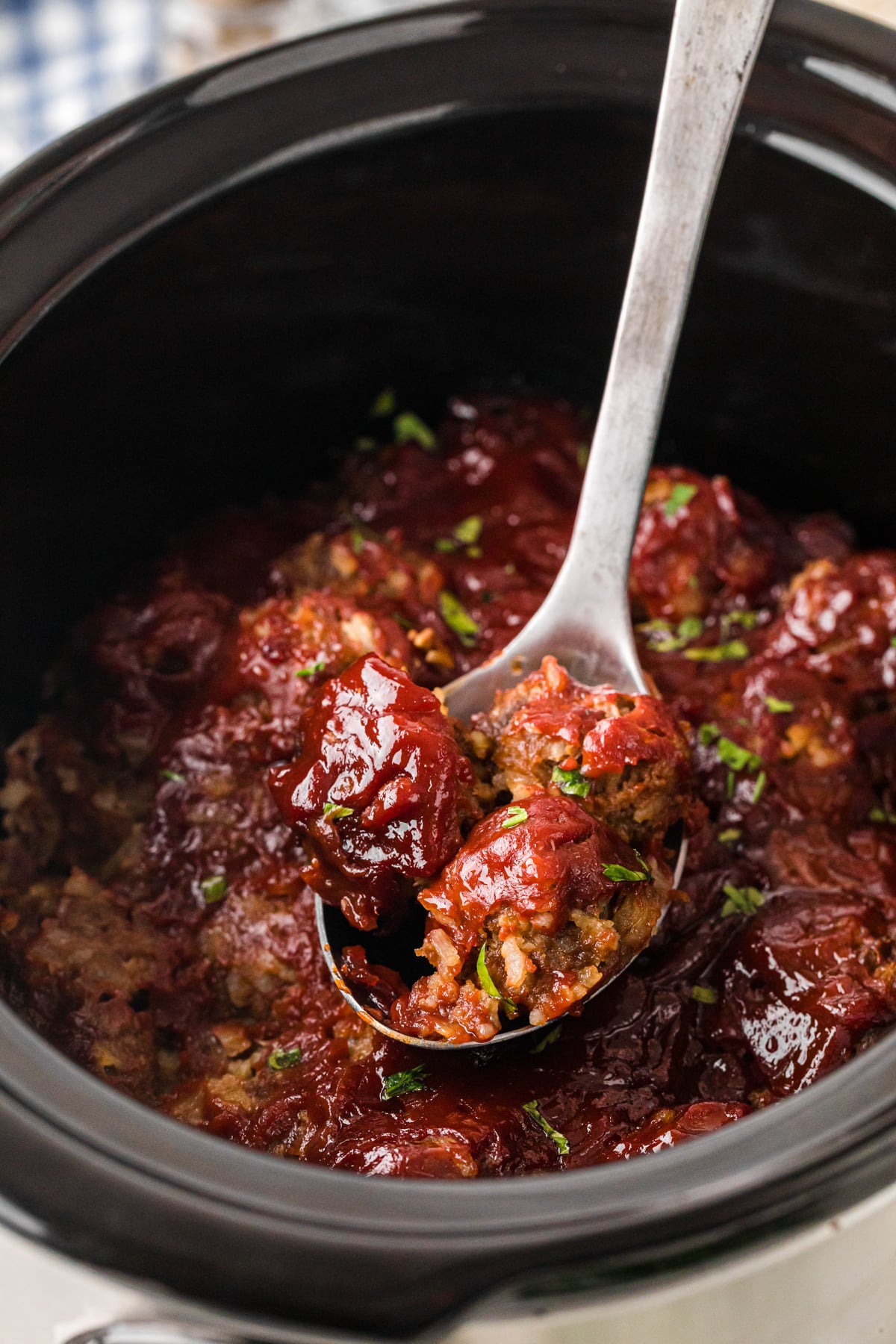 A big metal spoon scooping meatballs from a slow cooker.
